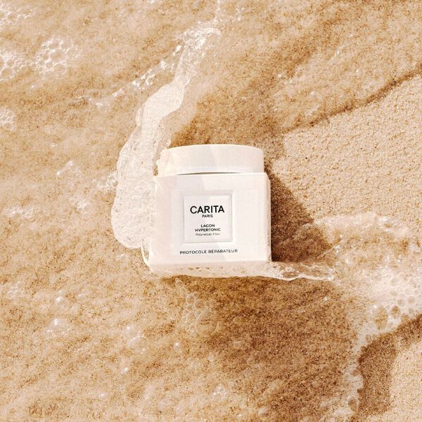 Pot blanc de Baume Lagon Carita pose dans le sable.