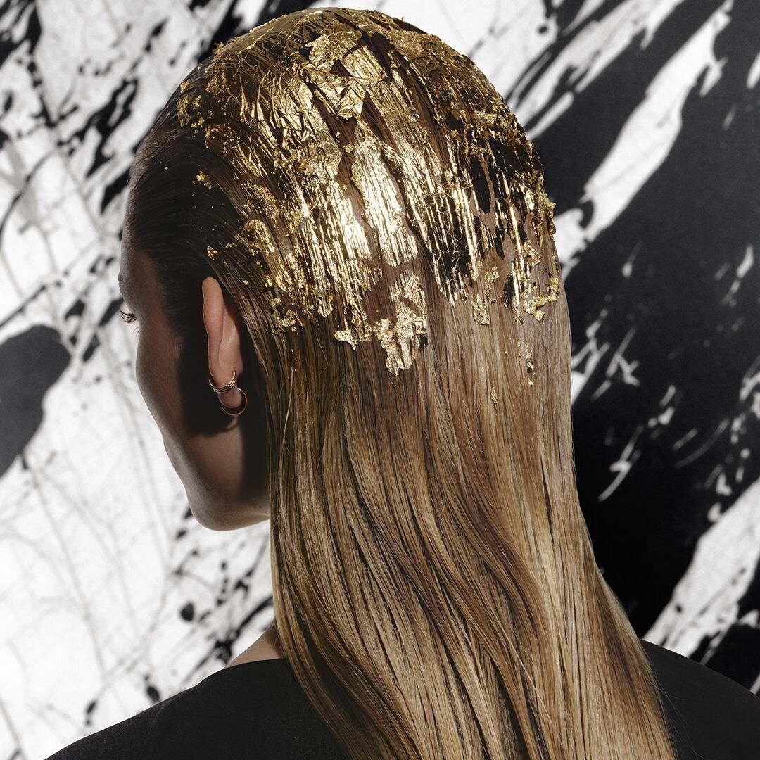 Femme blonde de dos, coiffee de feuilles d'or en peignoir noir Carita.