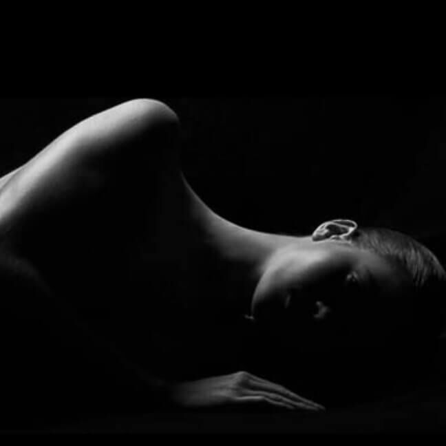 Silhouette d'une silhouette allongee sur fond noir, mettant en valeur les courbes et les lignes douces du corps.