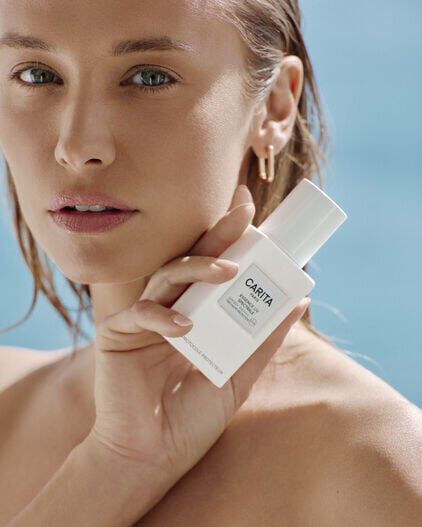 Portrait serre de femme tenant le flacon blanc d'Essence UV.