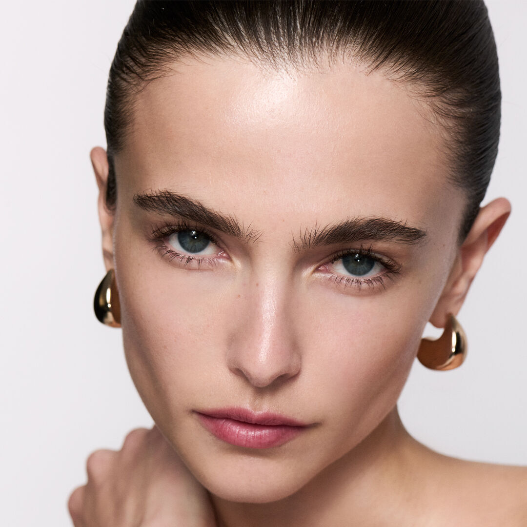 Femme brune aux cheveux plaques et boucles d'oreilles or.