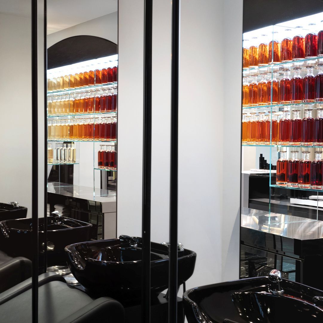 Salon de coiffure moderne et elegant avec des rangees de bouteilles de produits, des lavabos noirs brillants et des grands miroirs, offrant un cadre sophistique.