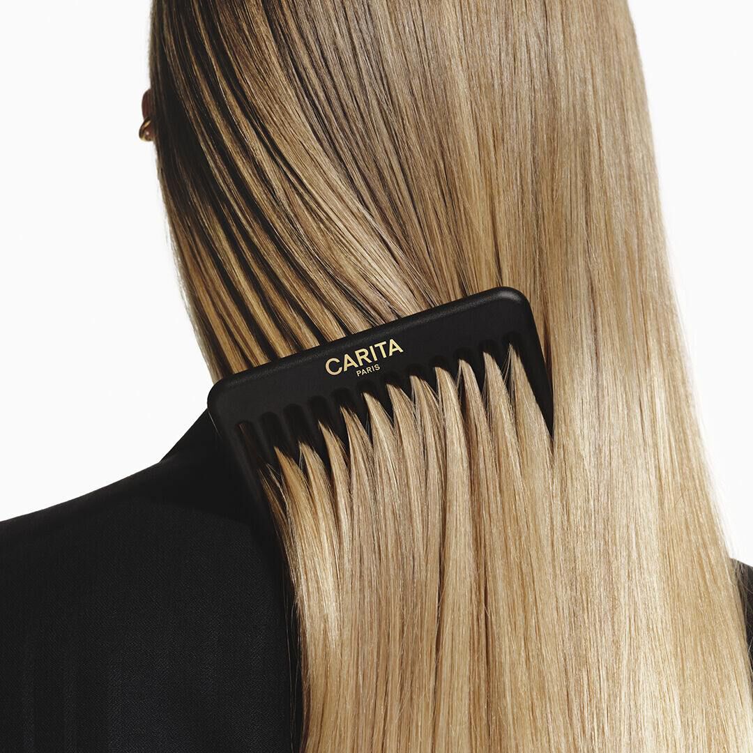 Peigne noir Carita demelant de longs cheveux blonds lisses.