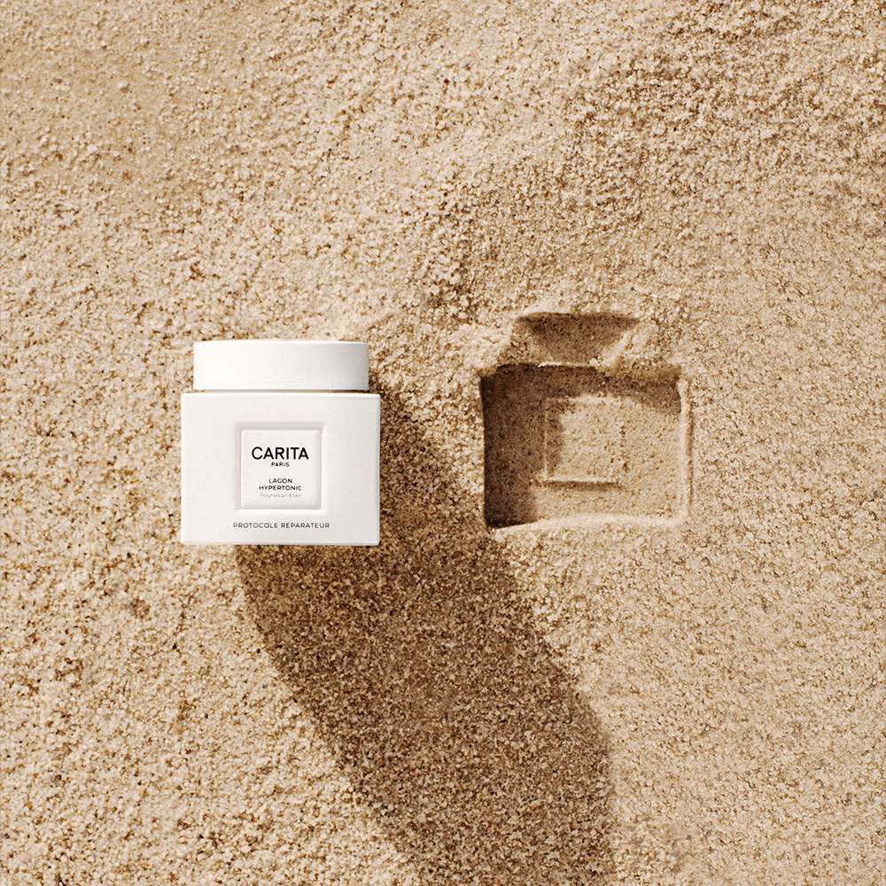 Creme pour le visage dans un pot blanc, dont la silhouette se detache sur un fond sable