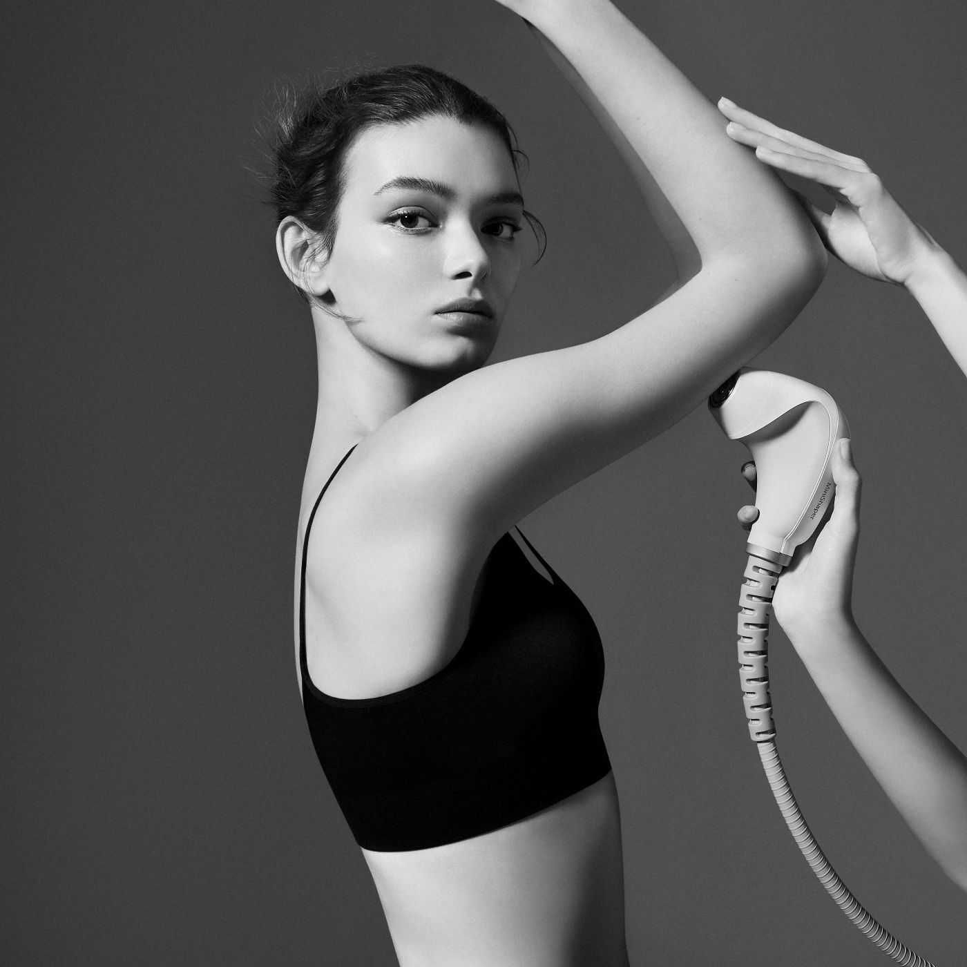 Une femme en noir et blanc recoit un traitement de beaute sur le bras a l'aide d'un appareil, avec une autre main qui la guide.