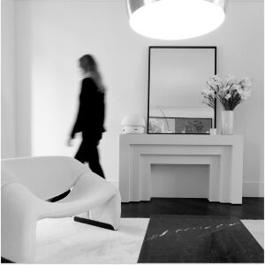 Interieur moderne et monochrome avec une personne en mouvement, une console elegante, un miroir, des fleurs et un fauteuil design blanc.