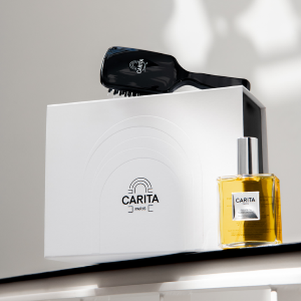 Elegante mise en scene de produits de beaute Carita Paris : brosse noire, boite blanche marquee et flacon d'huile doree, sur fond clair avec lumiere