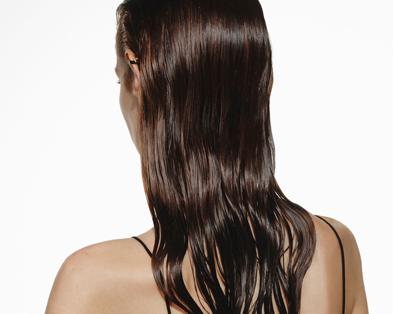 Dos d'une femme aux longs cheveux bruns humides et ondules.