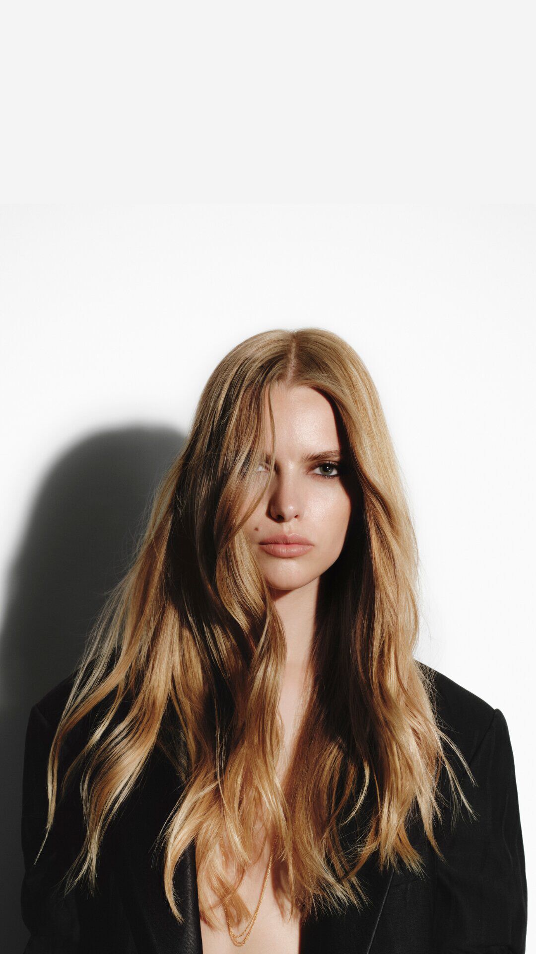 Femme blonde aux longs cheveux ondules en veste noire Carita.