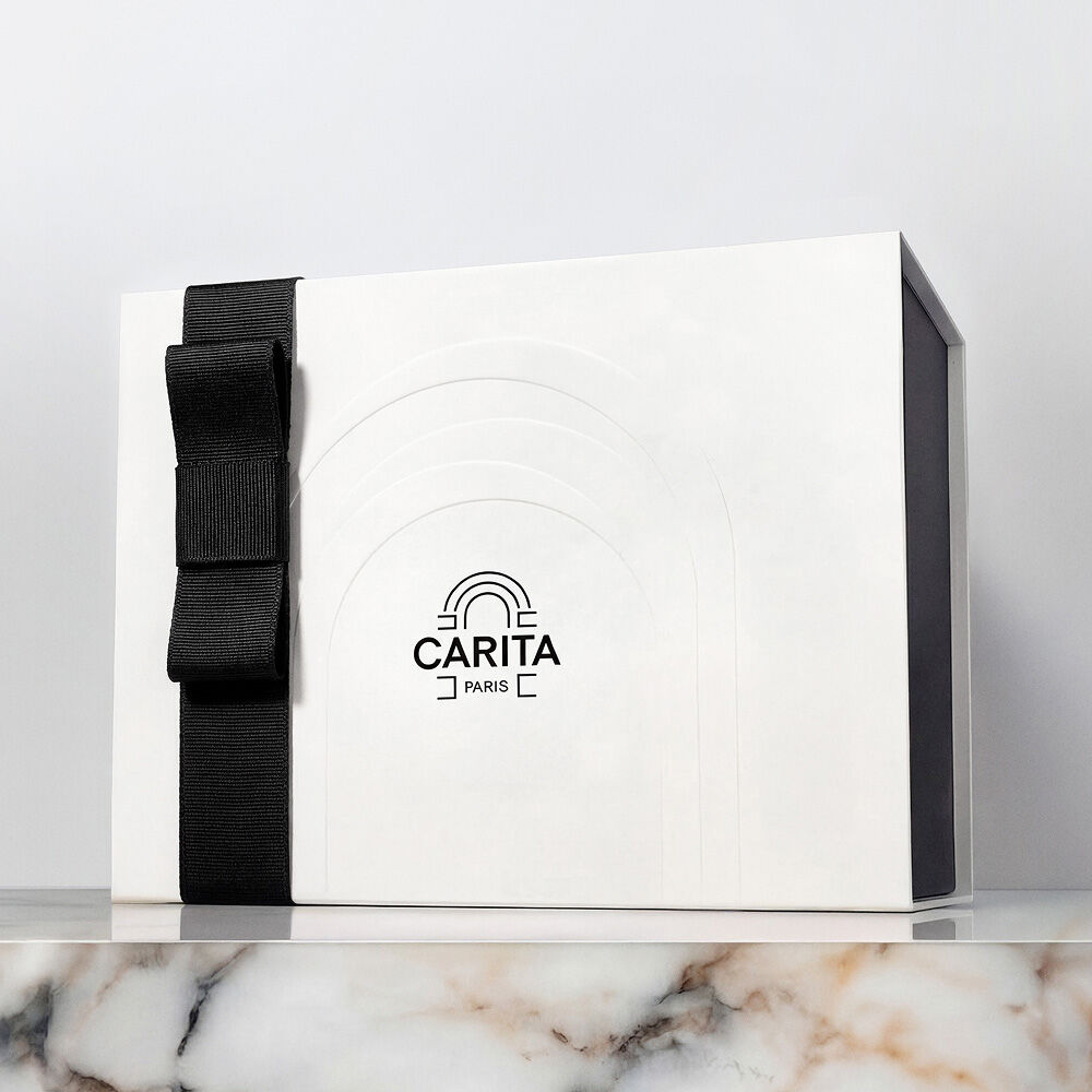 Un coffret cadeau de luxe Carita Paris blanc avec un elegant noeud en ruban noir, presente sur une surface en marbre.