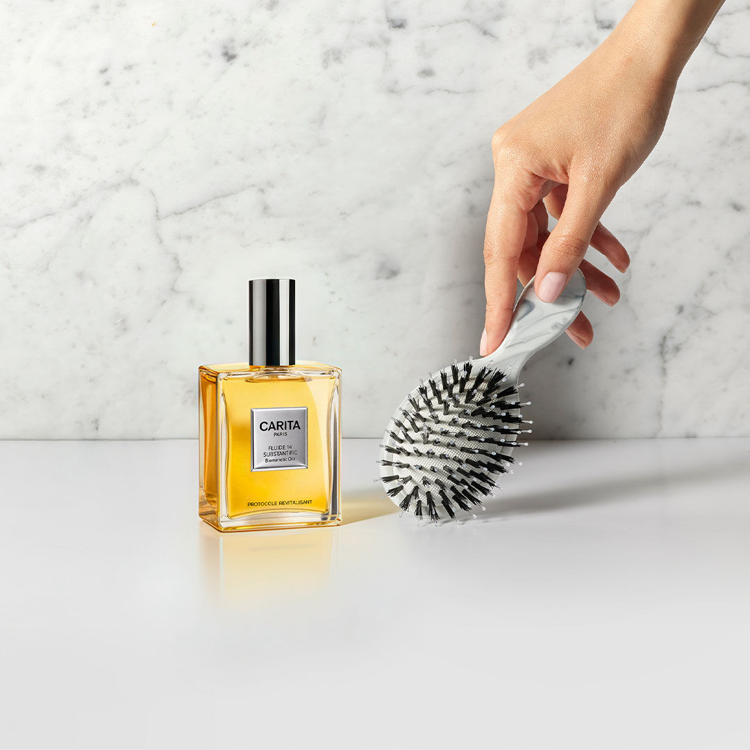 Flacon Carita Paris Fluide 14 a cote d'une main tenant une brosse marbree.​