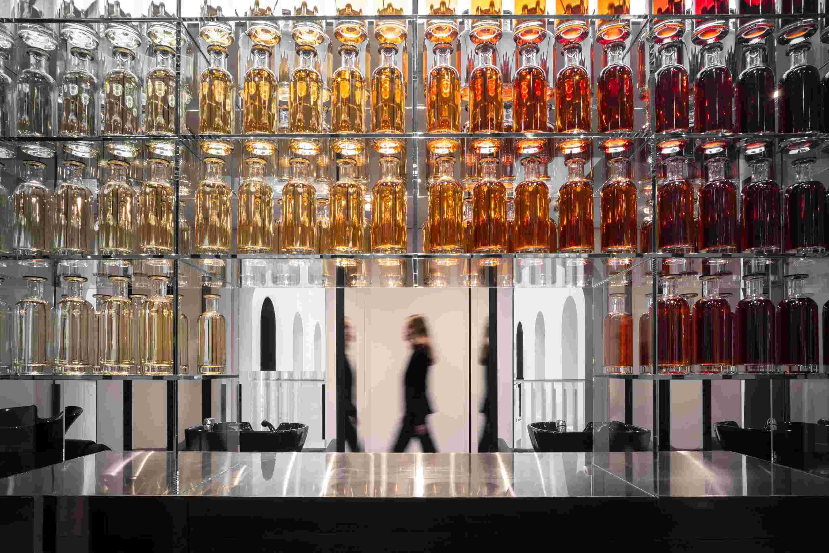 Flacons alignes et silhouettes marchant au salon 11 Faubourg.