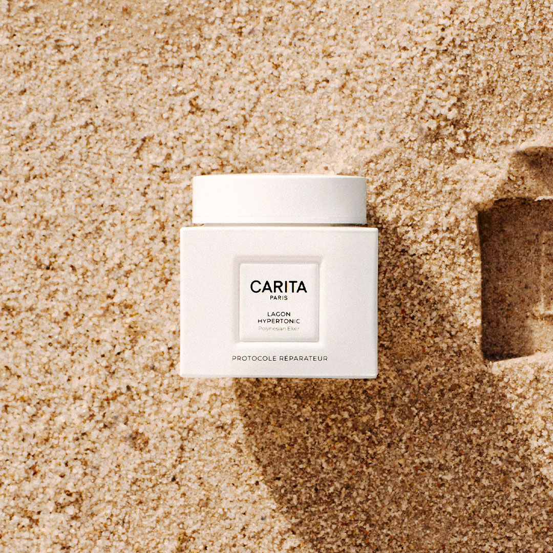 Pot de baume blanc Lagon Hypertonic pose sur du sable fin.