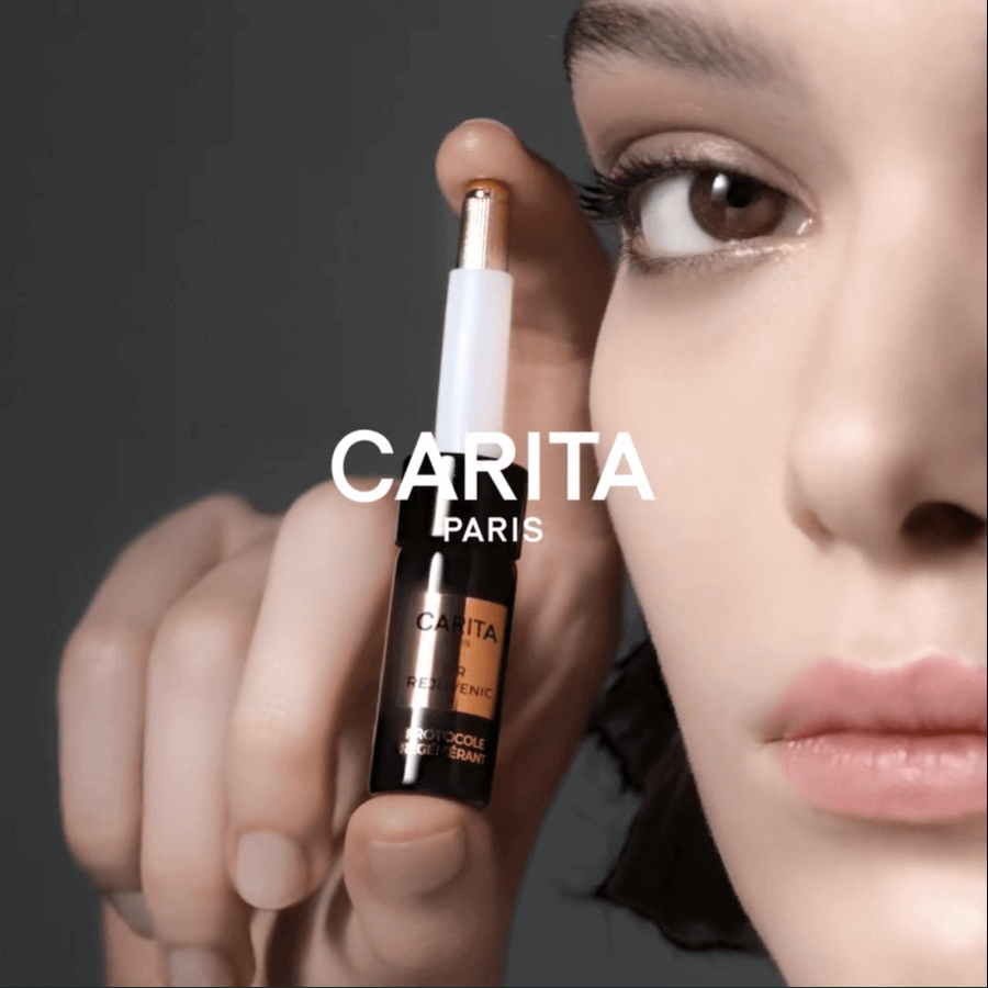 A close-up of a model's face showcasing a cosmetic product from Carita Paris, featuring a gold applicator tip and the brand's logo prominently displayed.