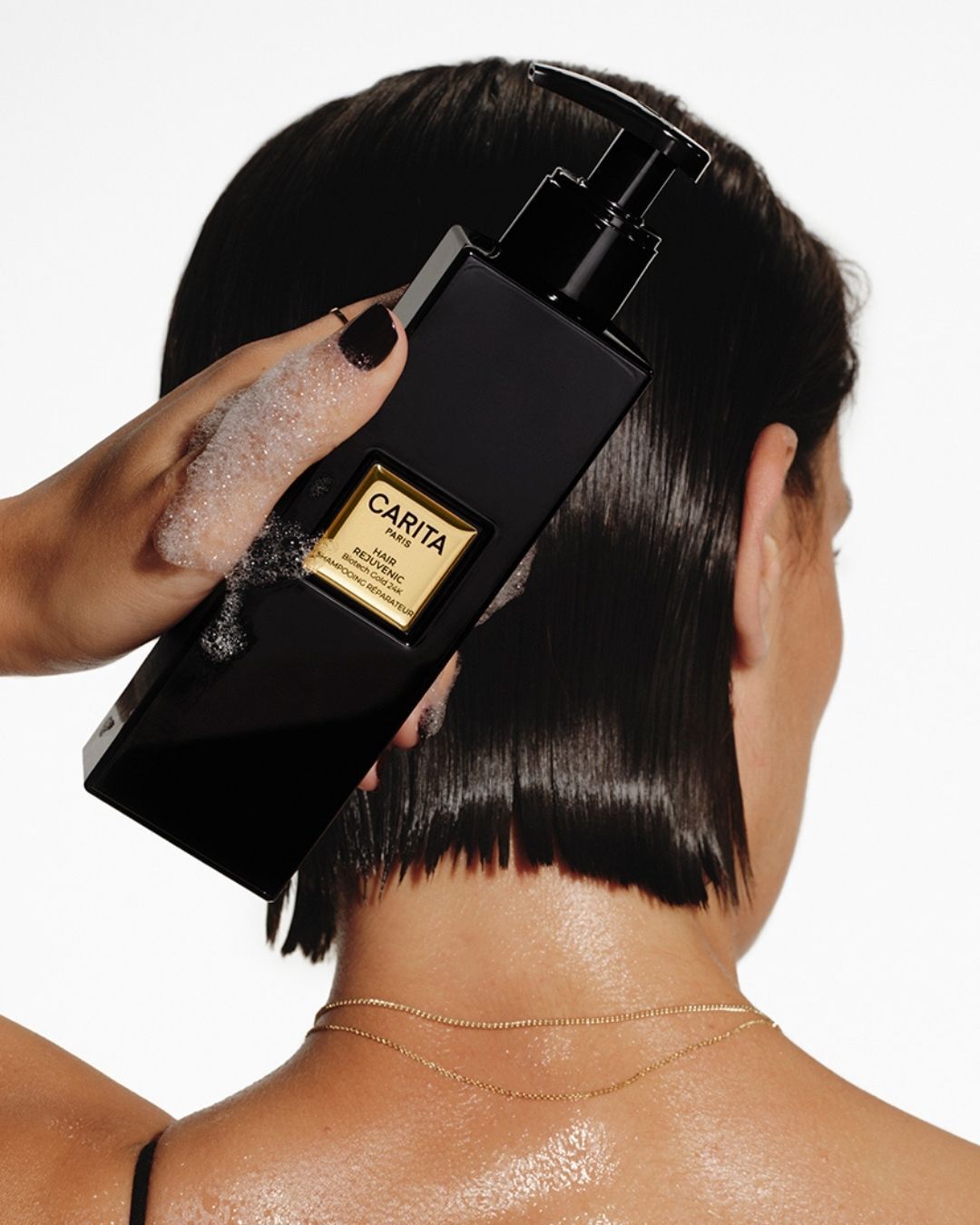 Femme aux cheveux courts tenant le Shampooing Reparateur Carita.
