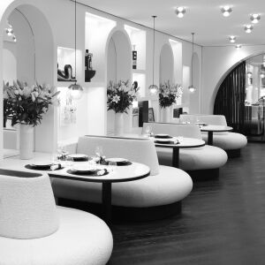 Interieur de restaurant elegant et moderne avec banquettes courbees, tables rondes dressees, et arches decoratives avec des fleurs.