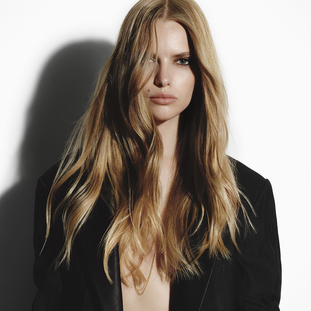 Femme blonde aux longs cheveux ondules en veste noire Carita.