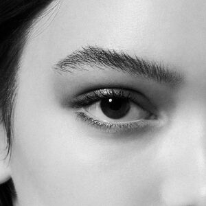 Gros plan monochrome intense sur un oeil feminin, mettant en evidence des cils volumineux et un sourcil defini, avec un point lumineux capte dans l'iris.