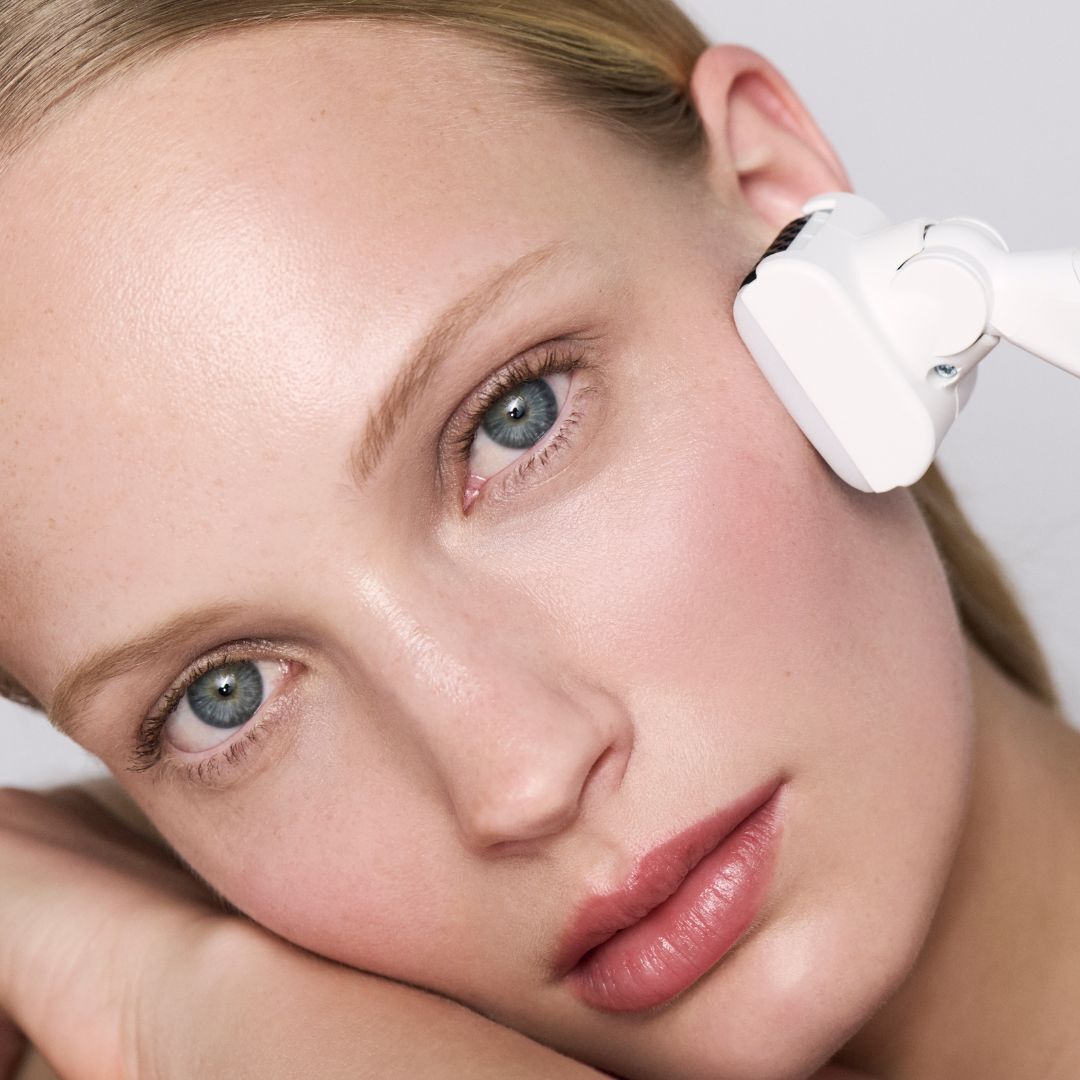 Femme recevant un soin du visage avec un appareil esthetique blanc.