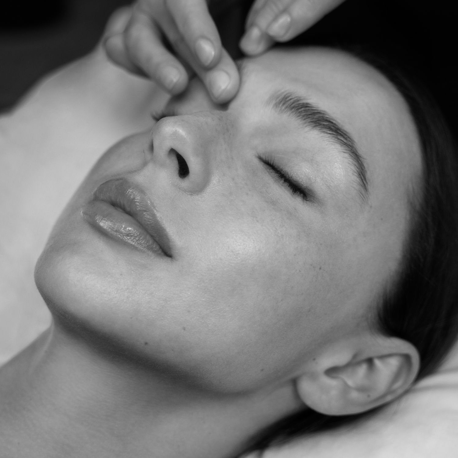 Gros plan monochrome d'une femme detendue recevant un massage du front, les yeux fermes. Ambiance de soin et de bien-etre.