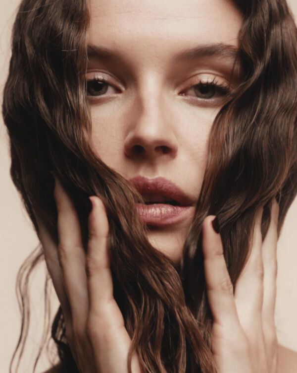 Femme brune de profil touchant ses cheveux.