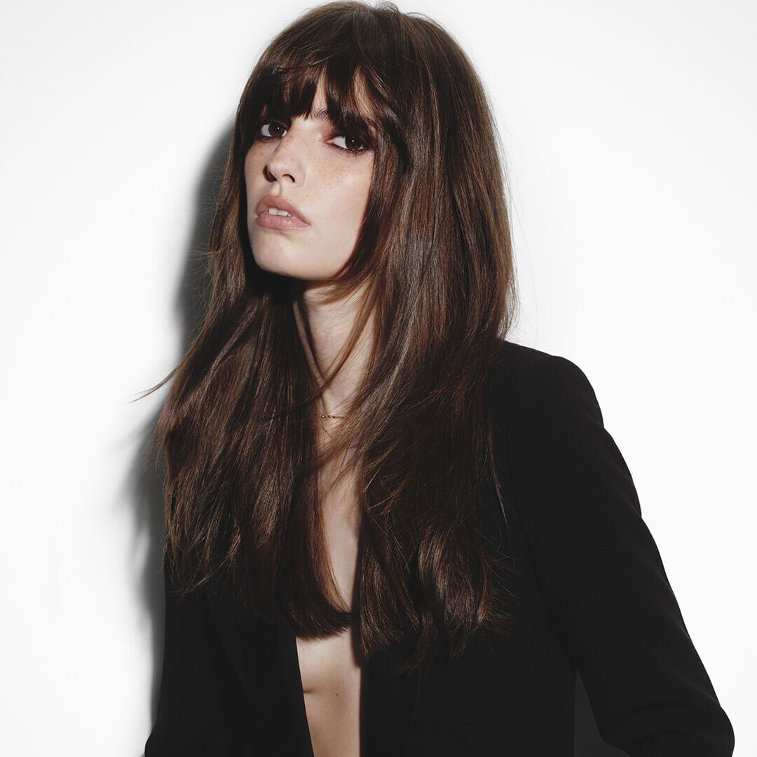 Femme brune a frange aux longs cheveux soyeux en veste noire.