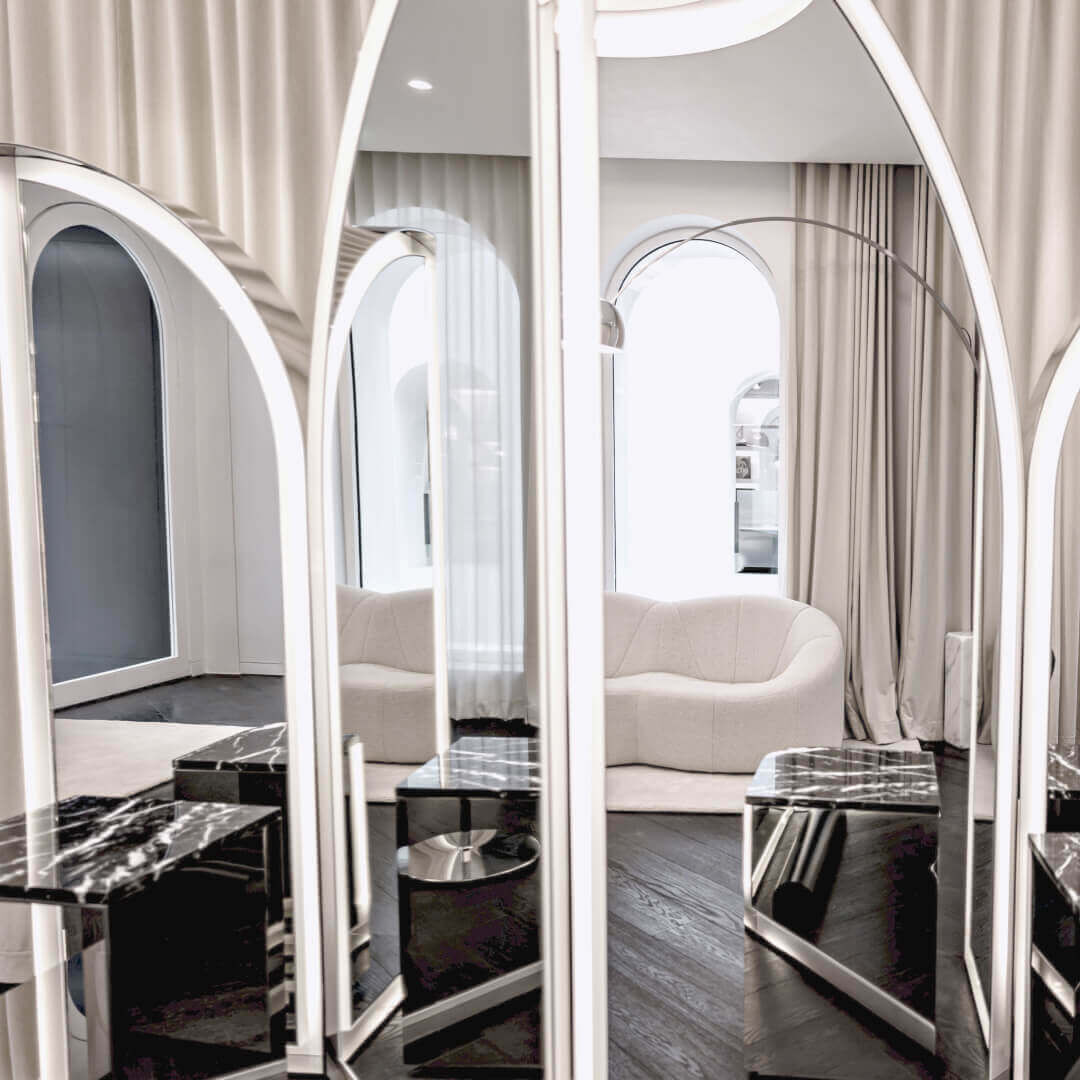 Cet interieur moderne et elegant presente des miroirs arques reflechissants avec eclairage lineaire. Des tables en marbre noir et un sol en parquet fonce y figurent. Un canape clair, des rideaux beiges et une lampe a arc creent une ambiance raffinee.