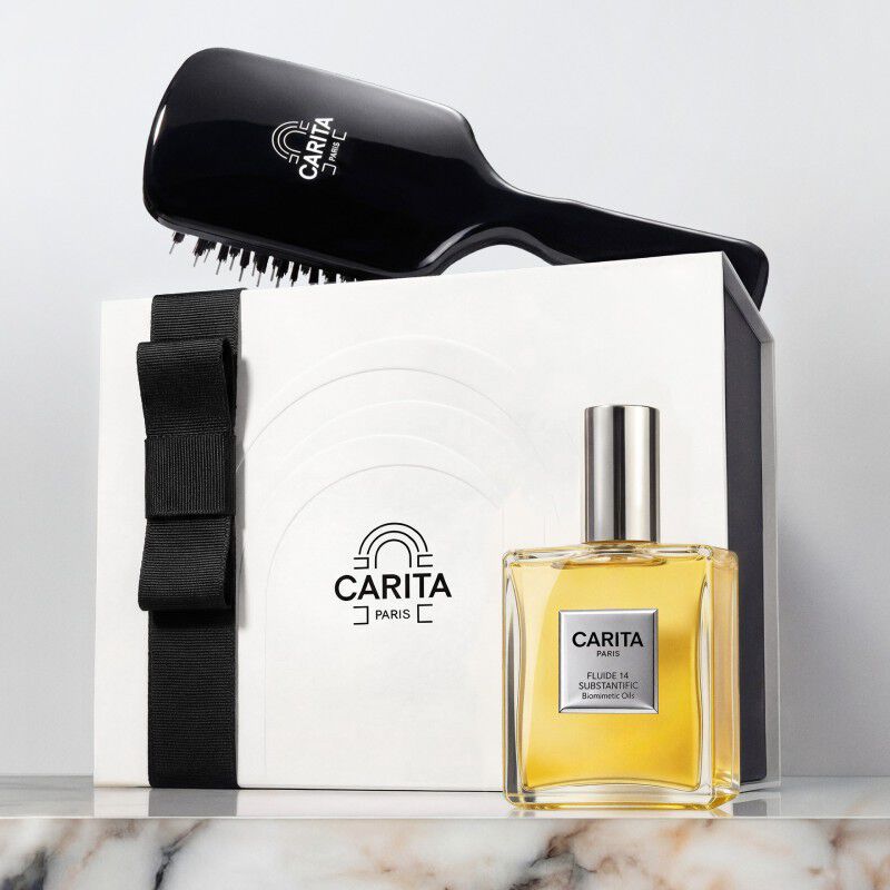 Coffret cadeau Carita Paris comprenant une brosse a cheveux noire, l'emblematique huile Fluide 14 et une boite cadeau blanche avec un ruban noir.