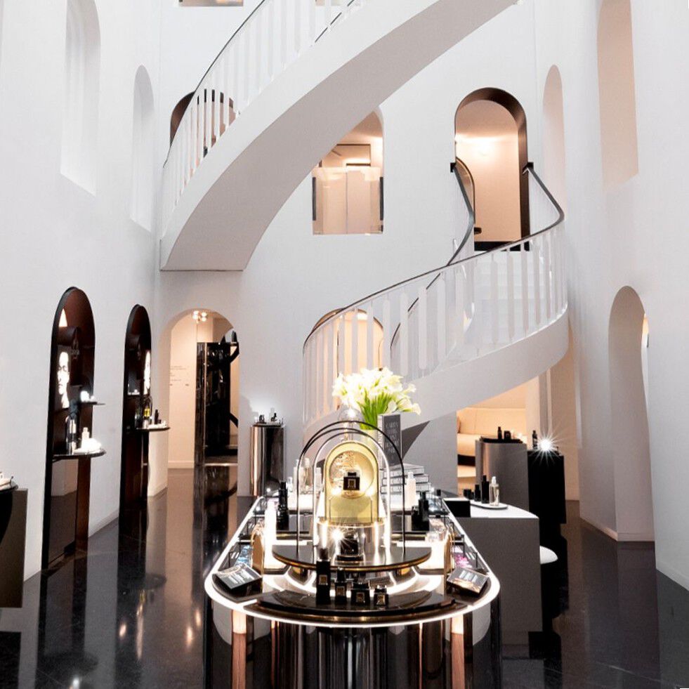 Maison de Beaute Carita : interieur moderne avec escalier blanc en spirale, murs arques et sol noir brillant, presentant des produits de beaute.